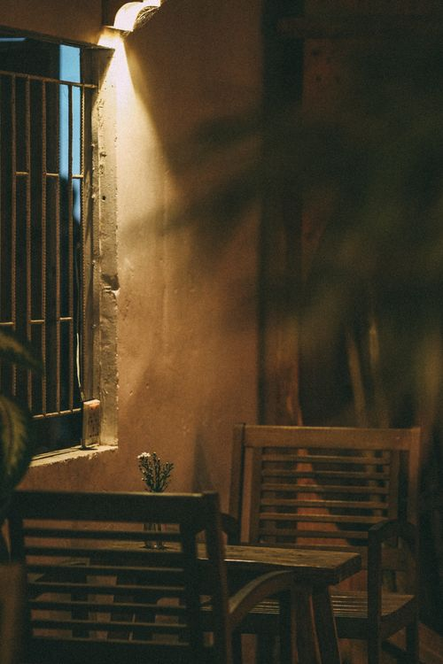 A third place at dusk — wrought-iron window, warm light, empty chairs waiting